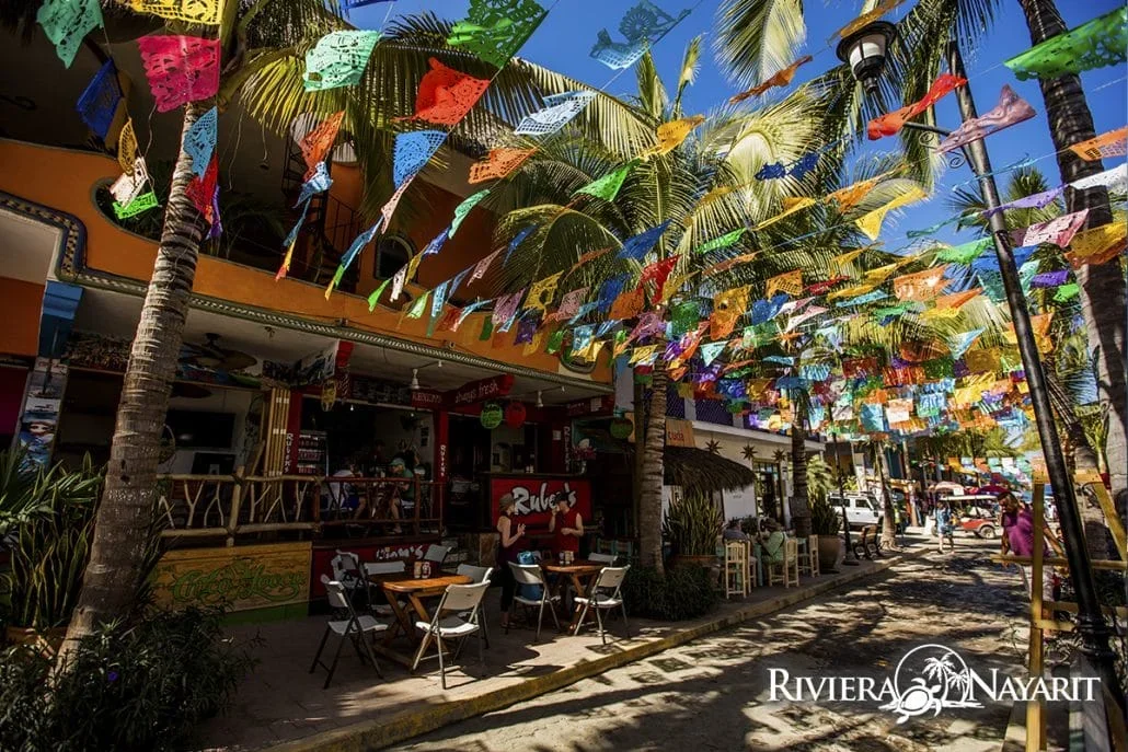 Calle de Sayulita cubierta de papel picado de colores con mesas al aire libre y palmeras