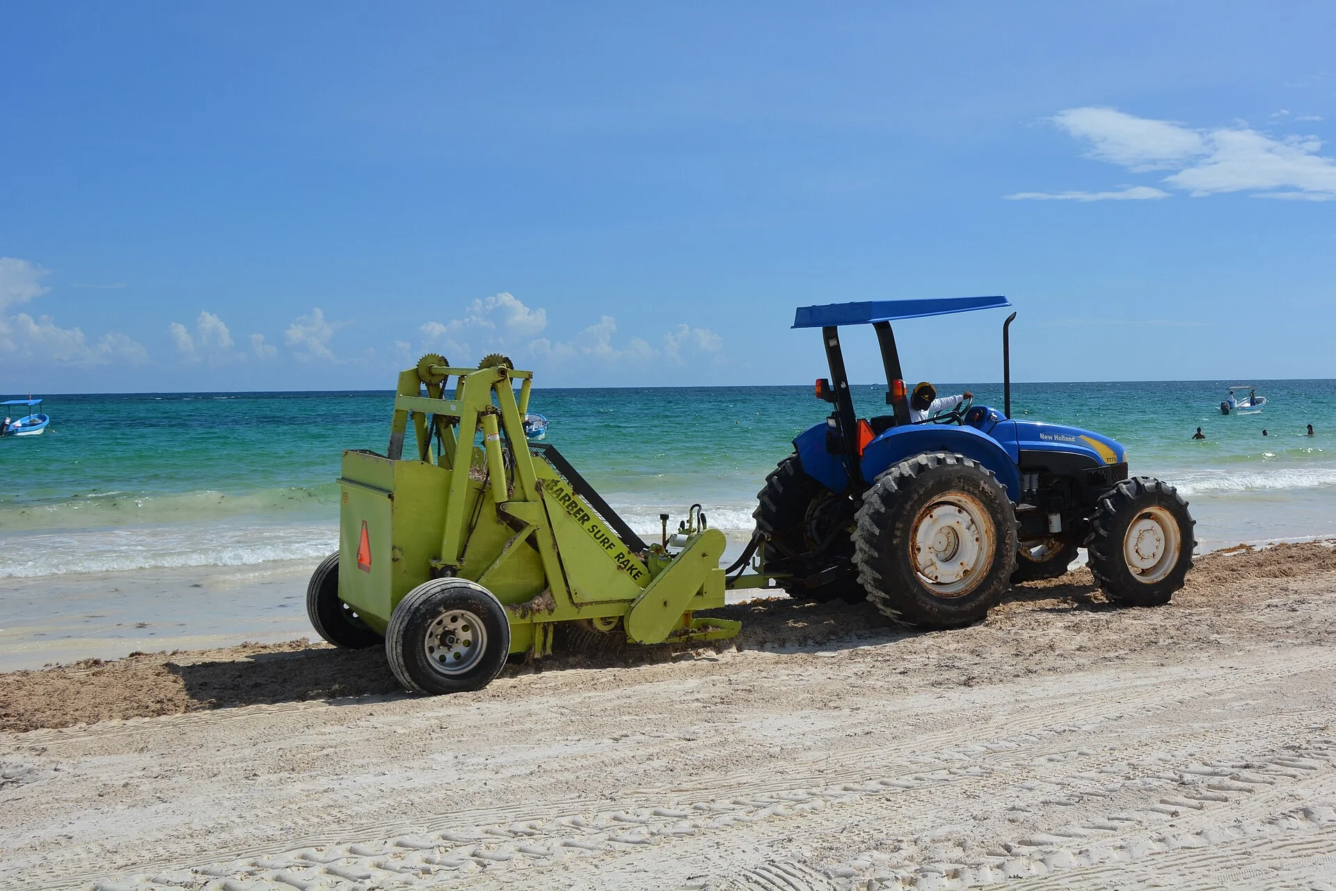 Tractor con máquina limpiadora de arena trabajando en una playa de Tulum frente al mar turquesa