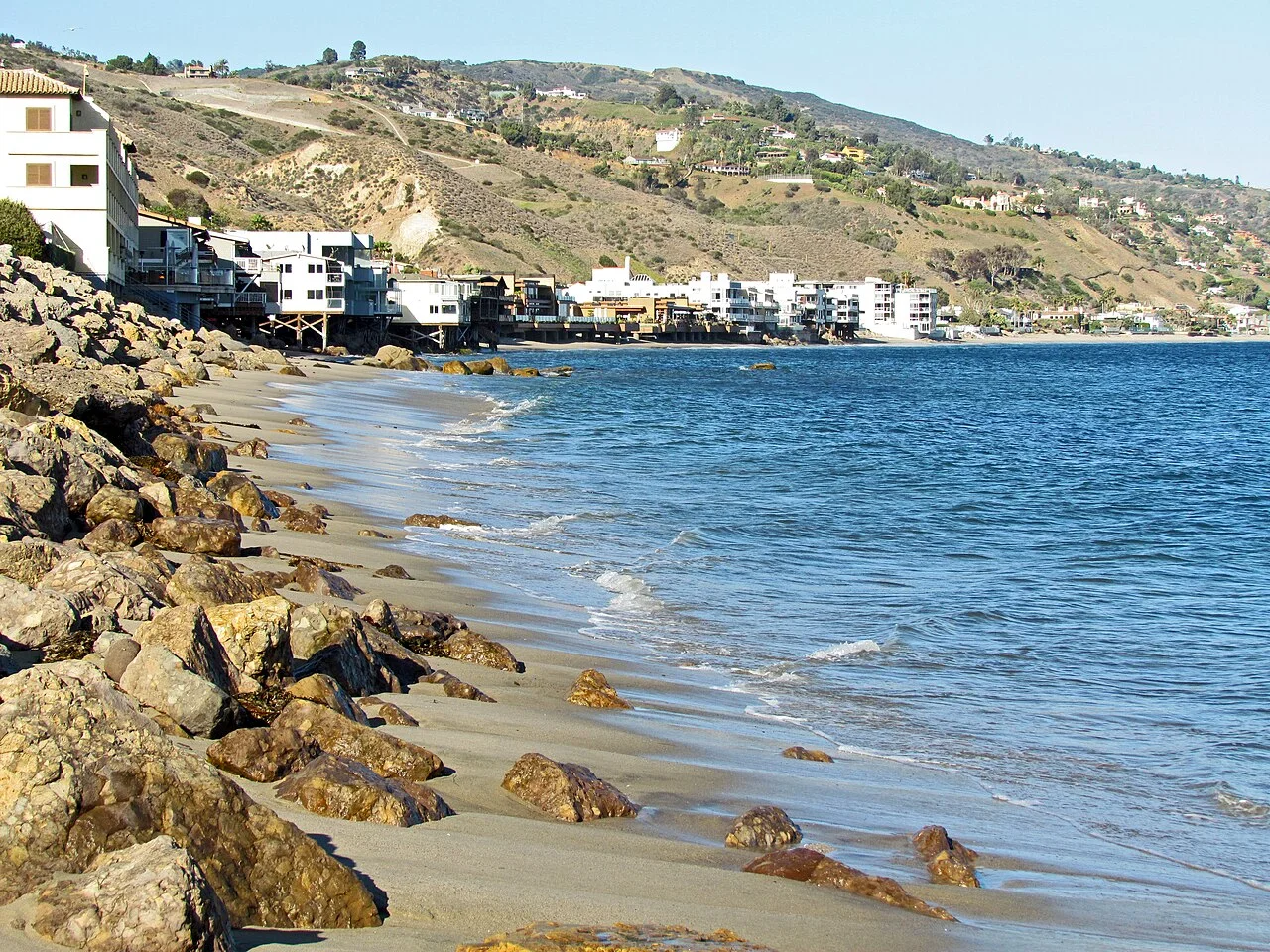 Playa rocosa de Malibú con casas frente al mar y colinas secas al fondo