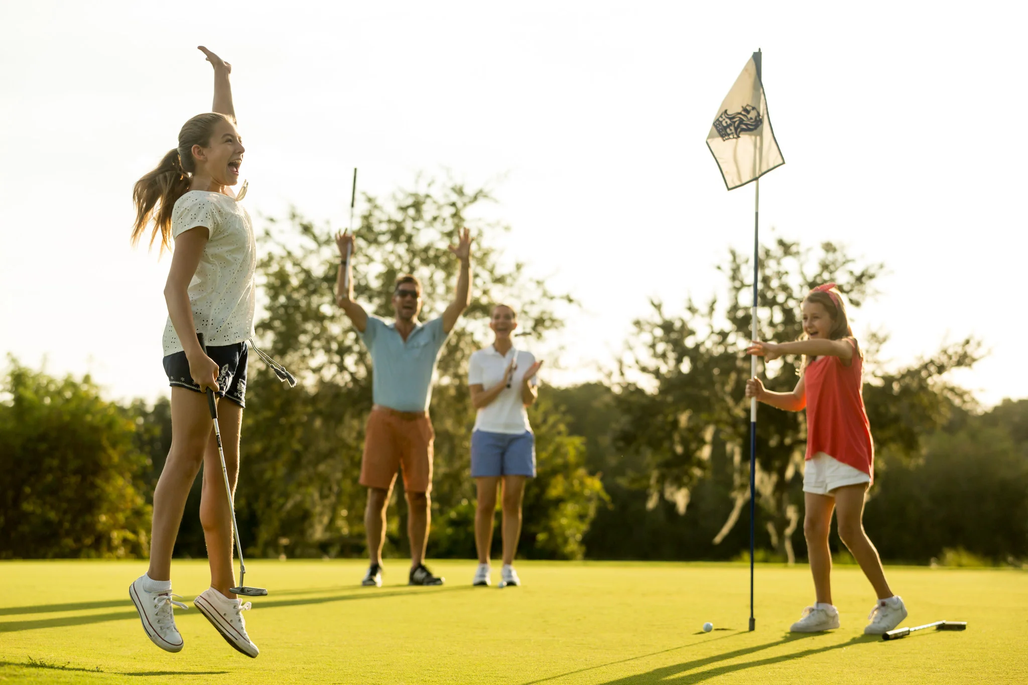 Niña salta de alegría en un green de golf mientras su familia aplaude junto al banderín