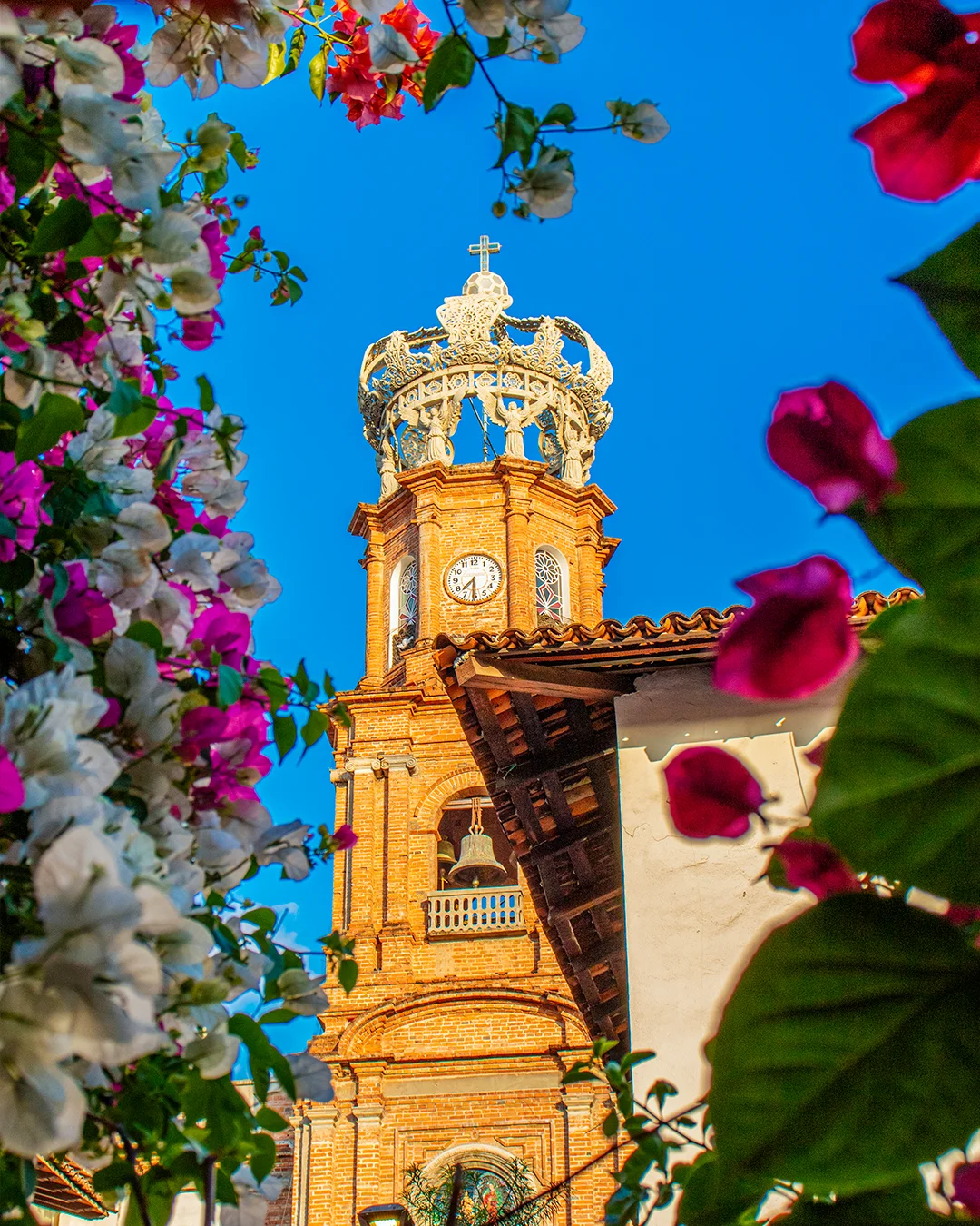 Torre de la Parroquia de Guadalupe con su corona blanca, enmarcada por buganvilias rosas y blancas bajo un cielo azul