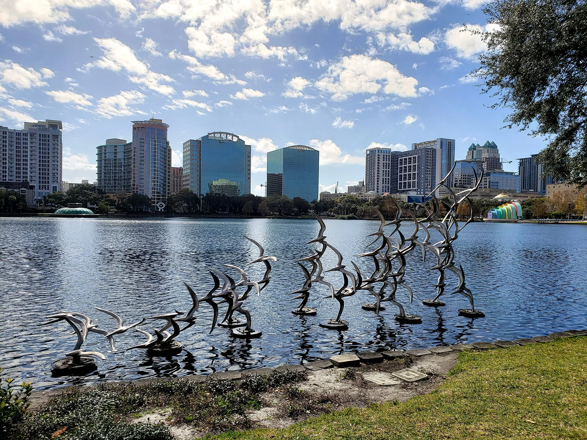 Esculturas metálicas de aves junto a la orilla del lago Eola con el horizonte de Orlando de fondo