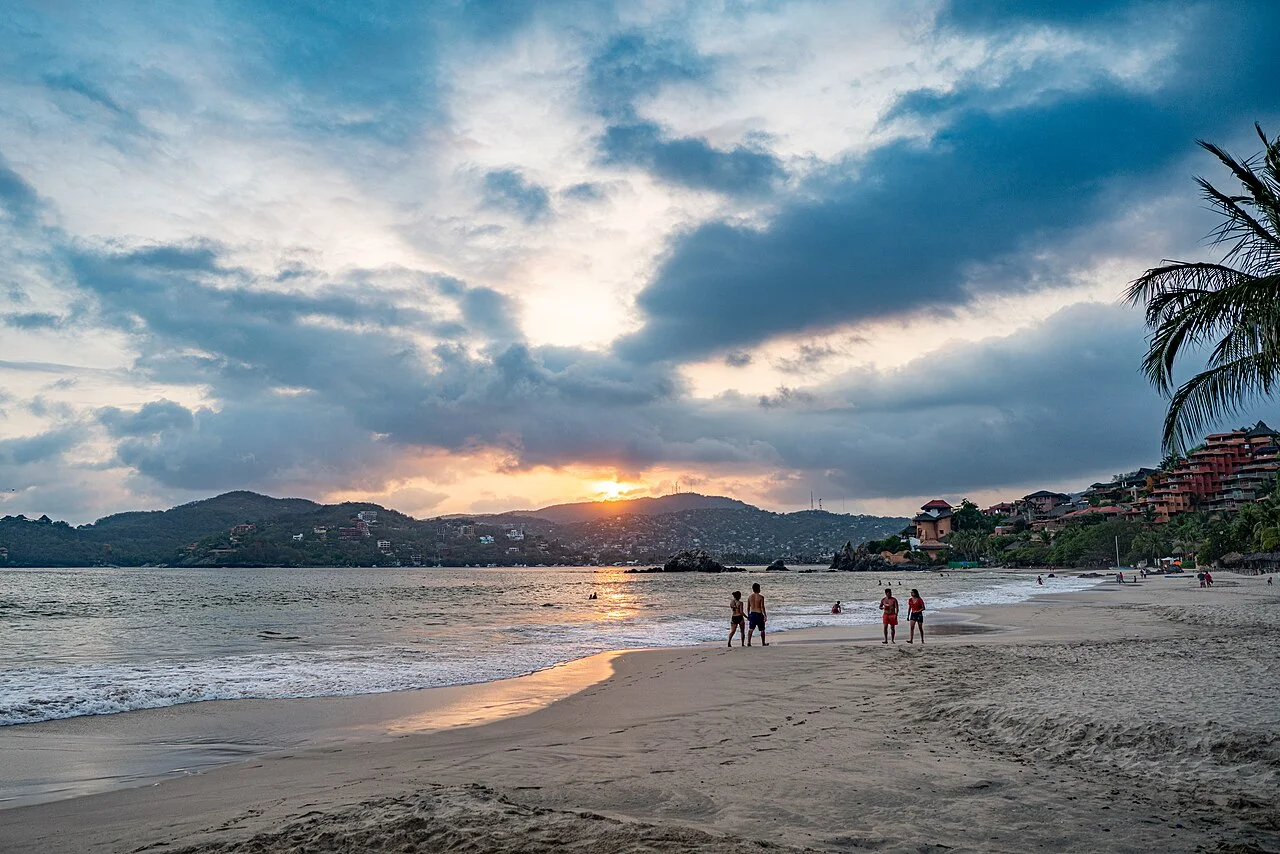 Playa La Ropa al atardecer, con gente caminando por la orilla y hoteles sobre el cerro
