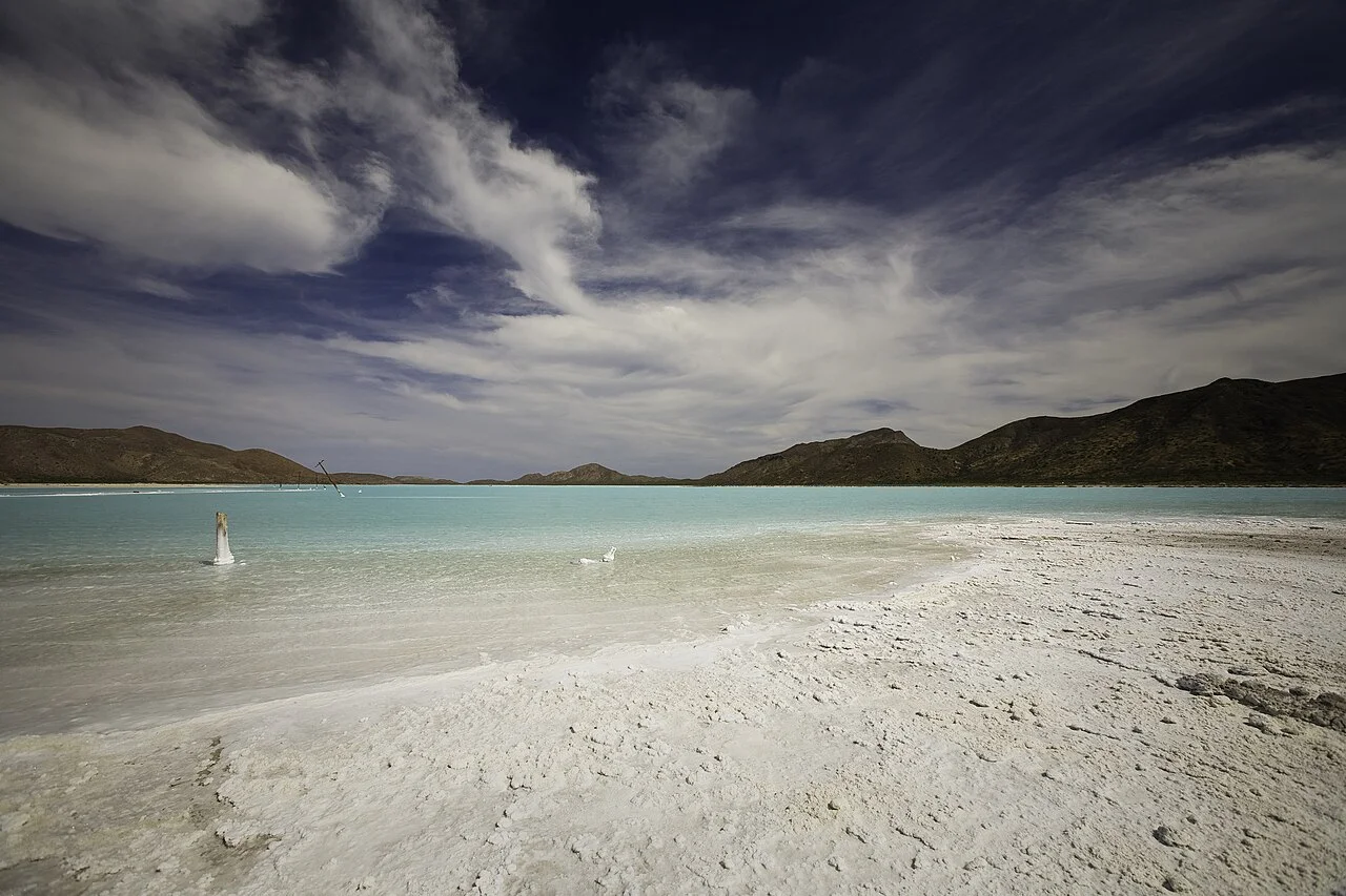 Salinera de costra blanca y agua turquesa rodeada de cerros en Isla del Carmen