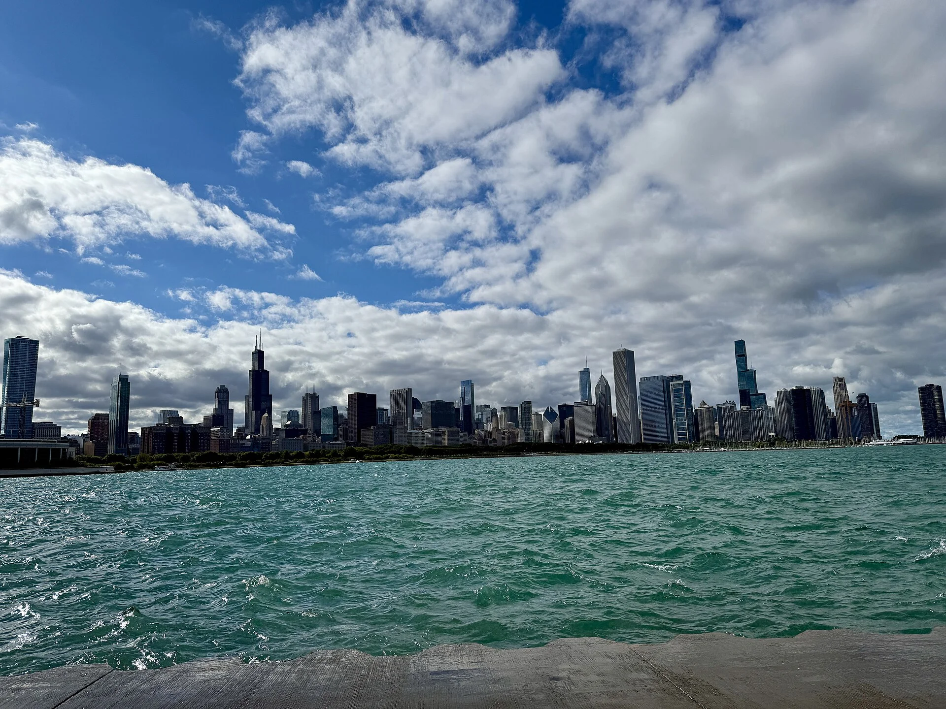Rascacielos de Chicago bajo nubes blancas, con el lago Michigan agitado en primer plano