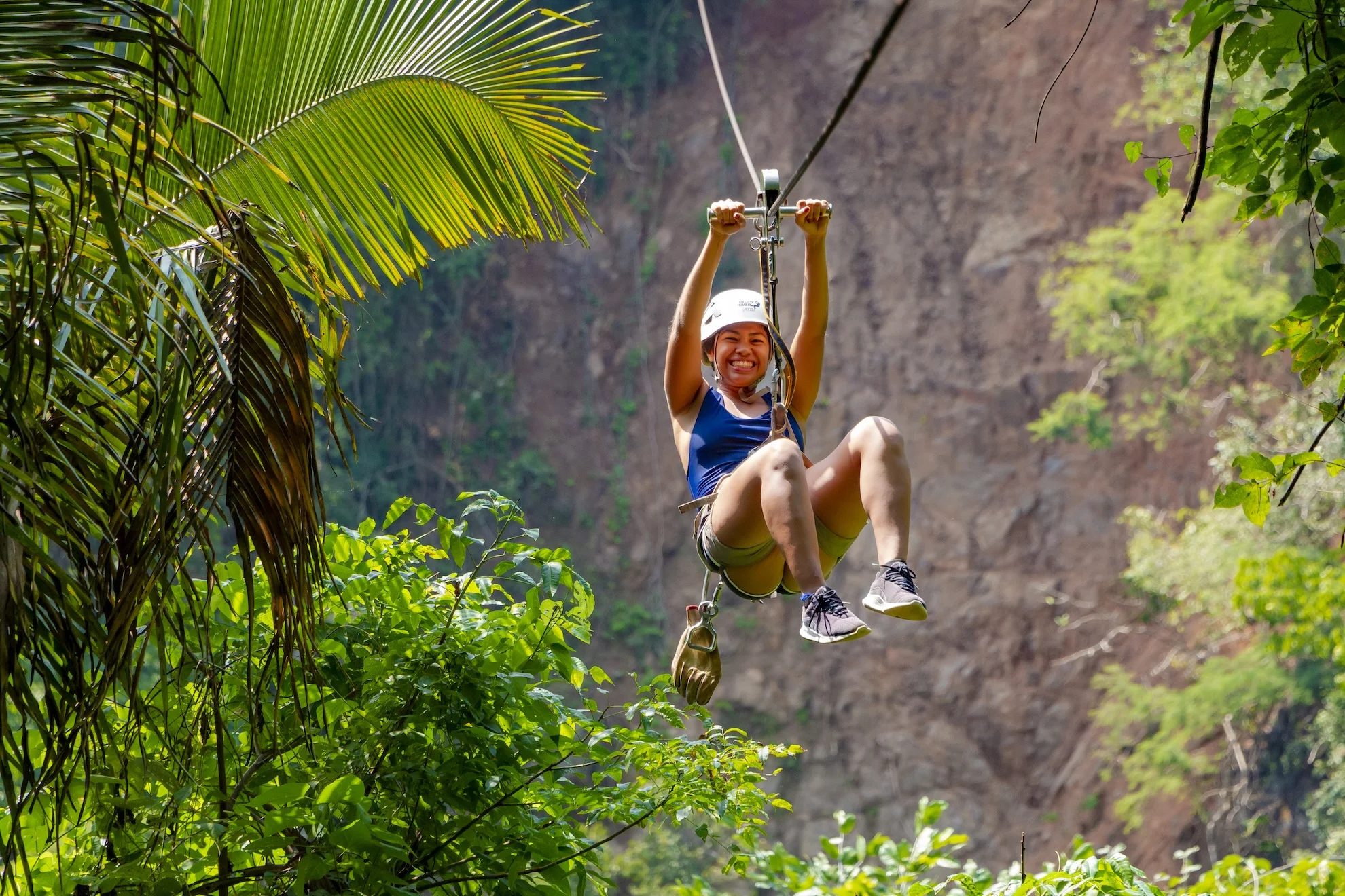 Persona sonriente en tirolesa sobre la selva tropical con una pared de roca al fondo