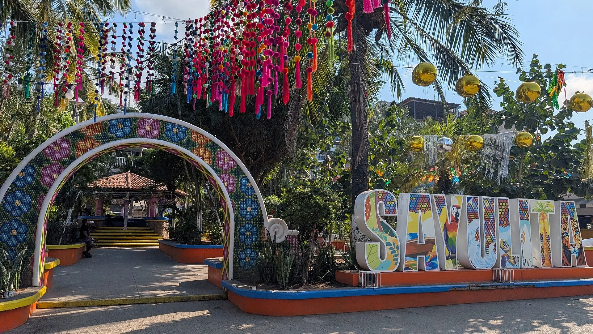 Letras coloridas de Sayulita bajo papel picado y arco decorado en la entrada de la plaza