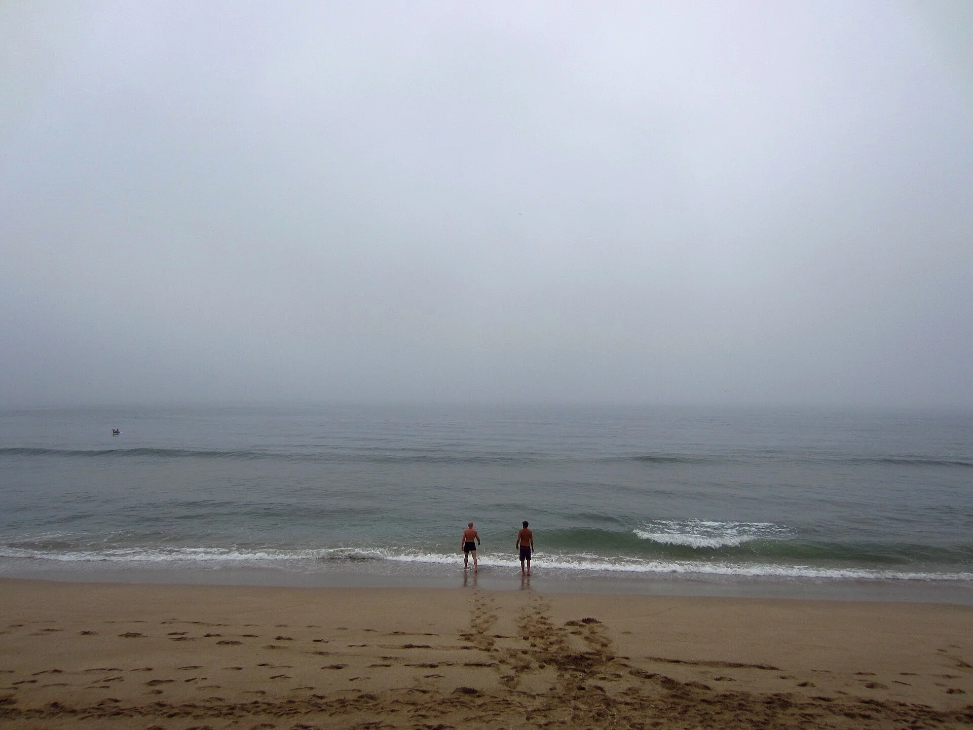 Dos personas entrando al mar en una playa de Mazatlán en una mañana nublada