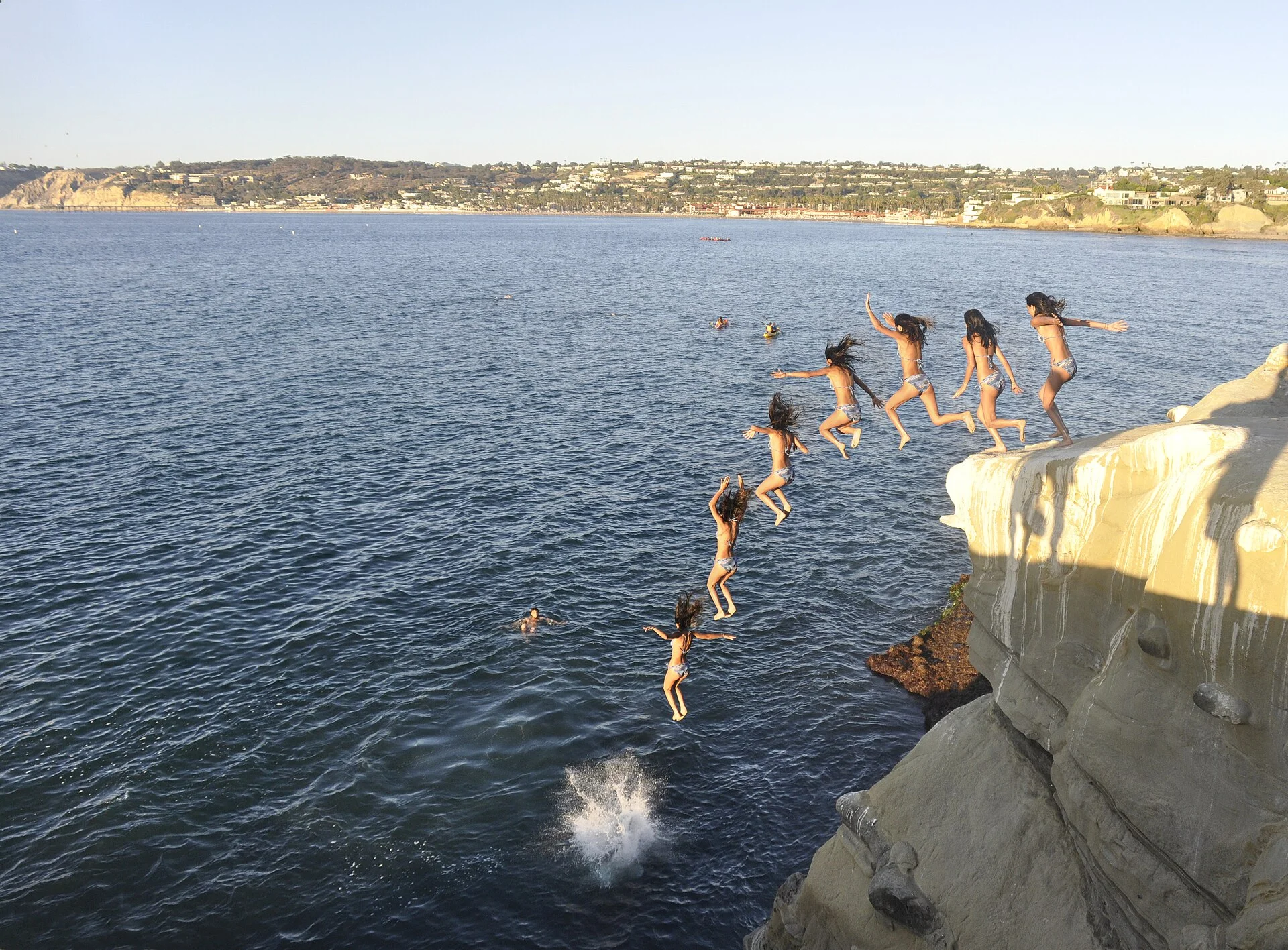 Grupo de jóvenes saltando al mar desde un acantilado de arenisca en la costa de San Diego