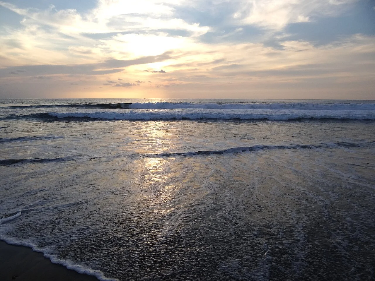 Olas rompiendo en Playa Zicatela al atardecer, con el reflejo del sol sobre la arena mojada