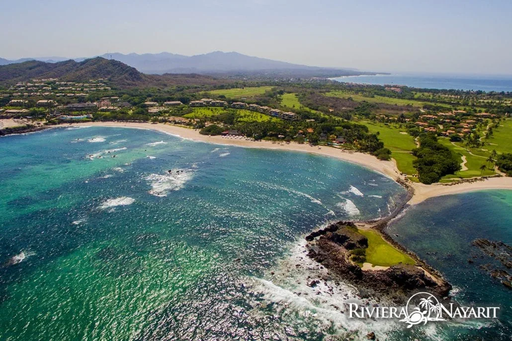 Vista aérea de Punta de Mita con campo de golf, playa de arena y un islote verde en el mar