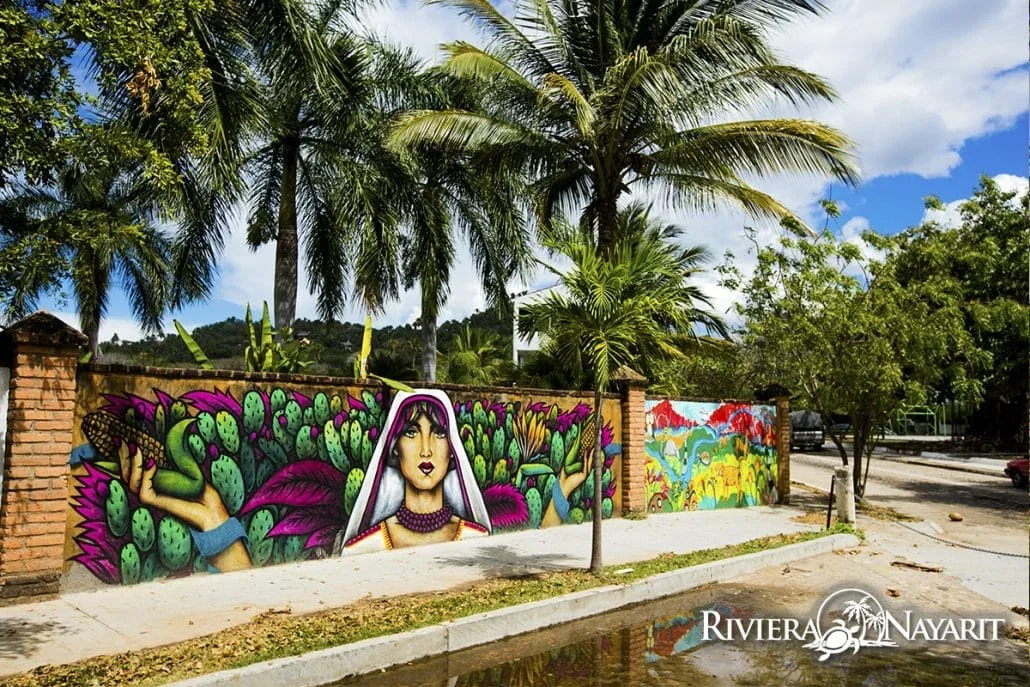 Mural colorido con figura de mujer y cactus en una calle con palmeras de la costa nayarita