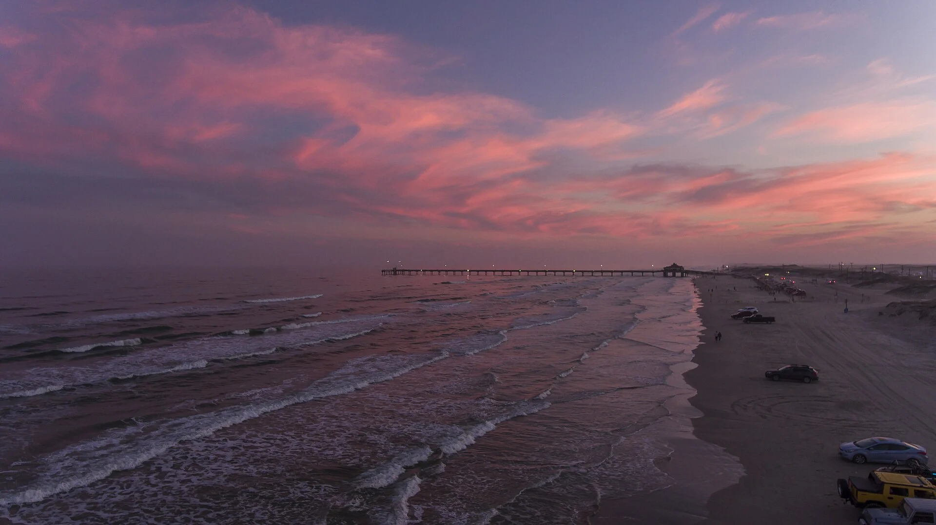 Vista aérea de un atardecer rosado sobre el Golfo de México con un muelle de pesca en la orilla