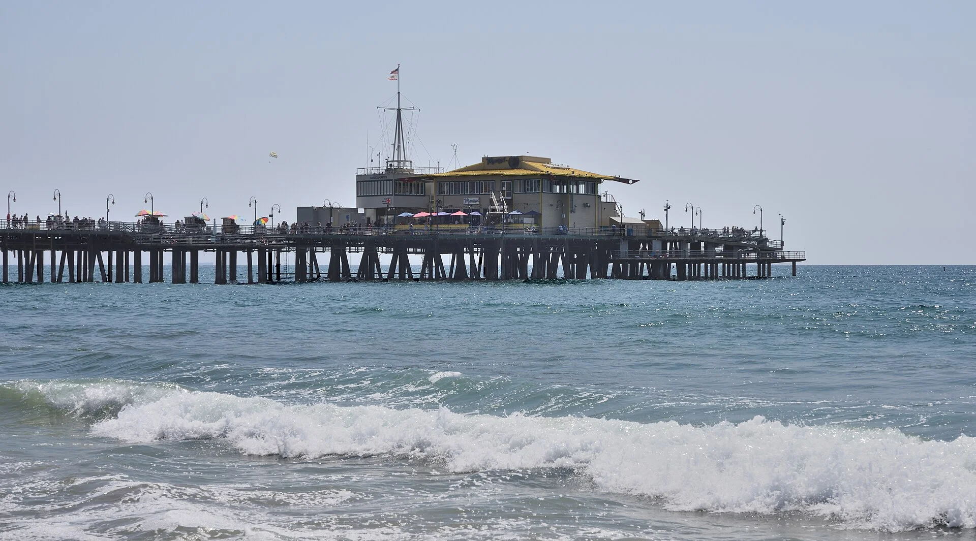 Extremo del muelle de Santa Mónica sobre pilotes de madera visto desde el agua, con olas rompiendo