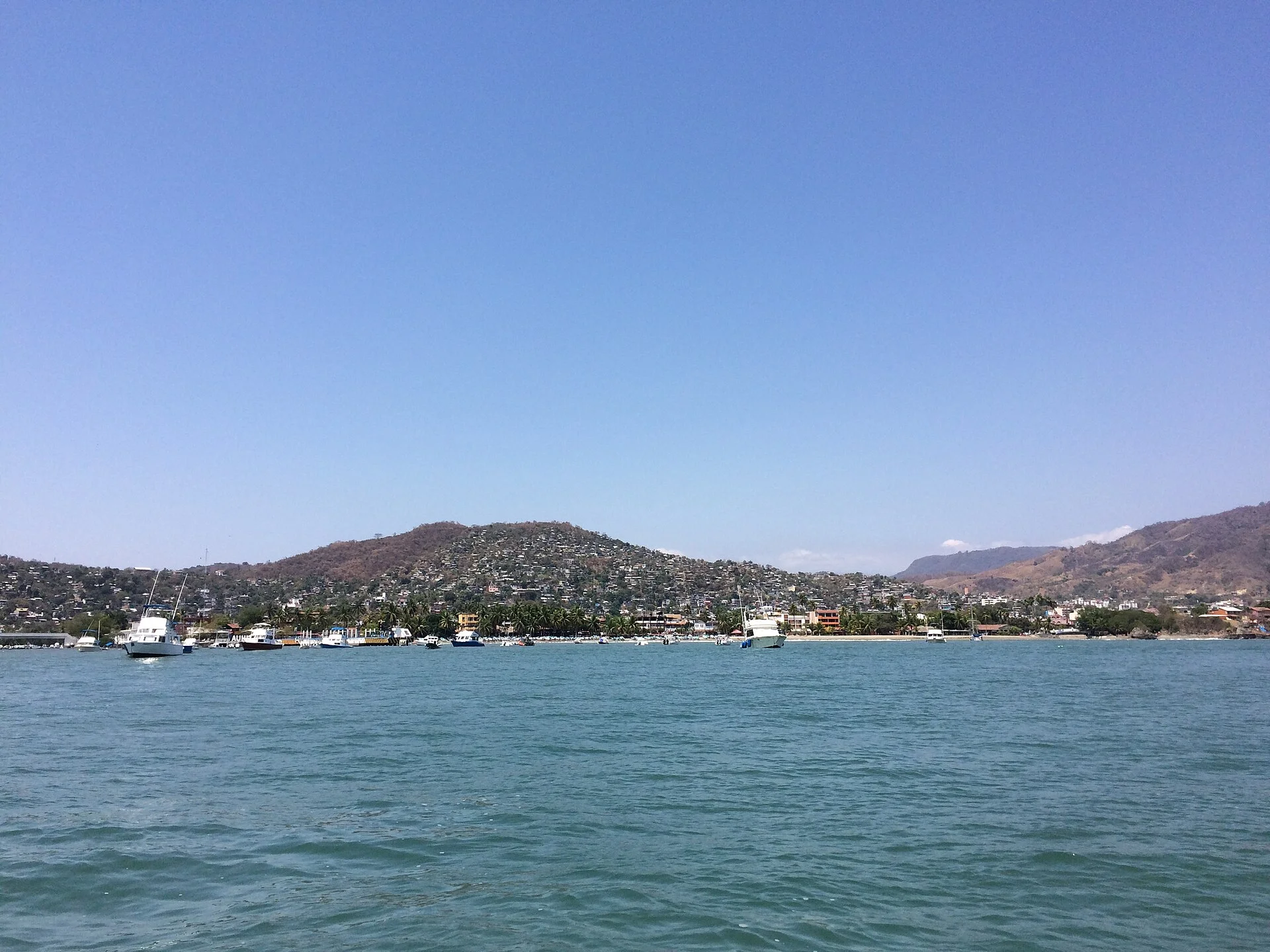 Zihuatanejo visto desde el agua, con lanchas frente a la playa y el pueblo sobre los cerros