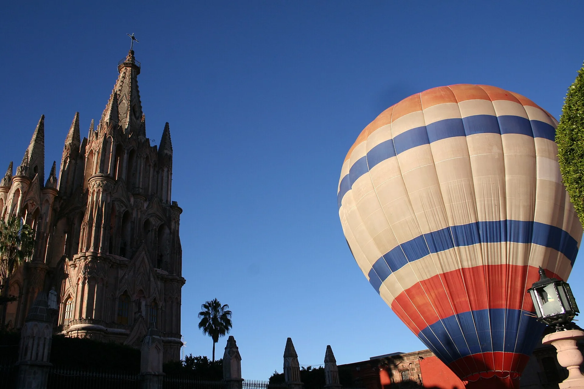 Globo aerostático a rayas inflándose junto a la Parroquia de San Miguel Arcángel con cielo azul