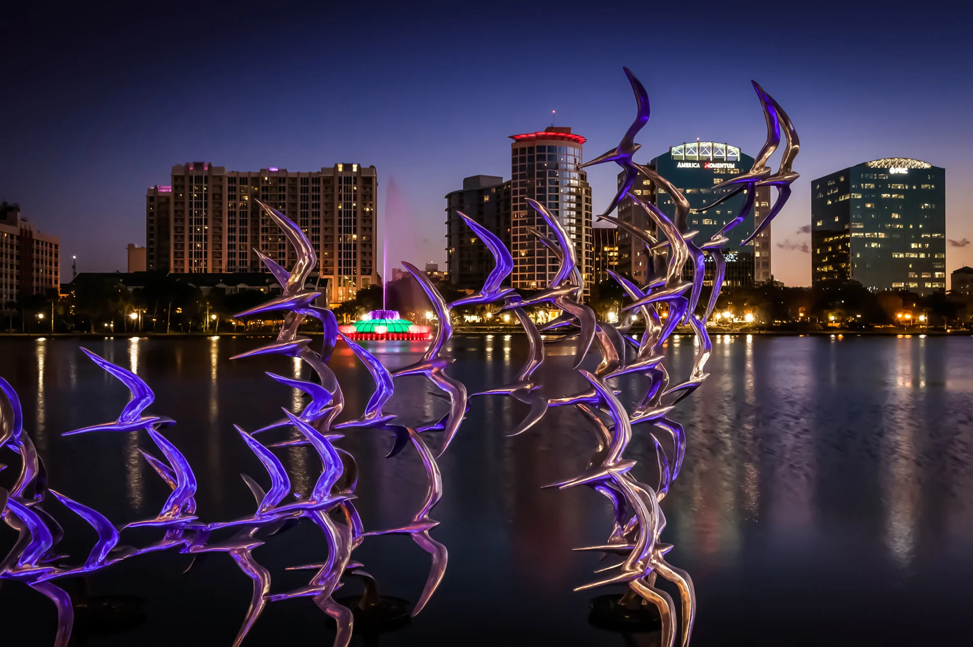 Esculturas iluminadas de aves en el lago Eola con los edificios del centro de Orlando de noche