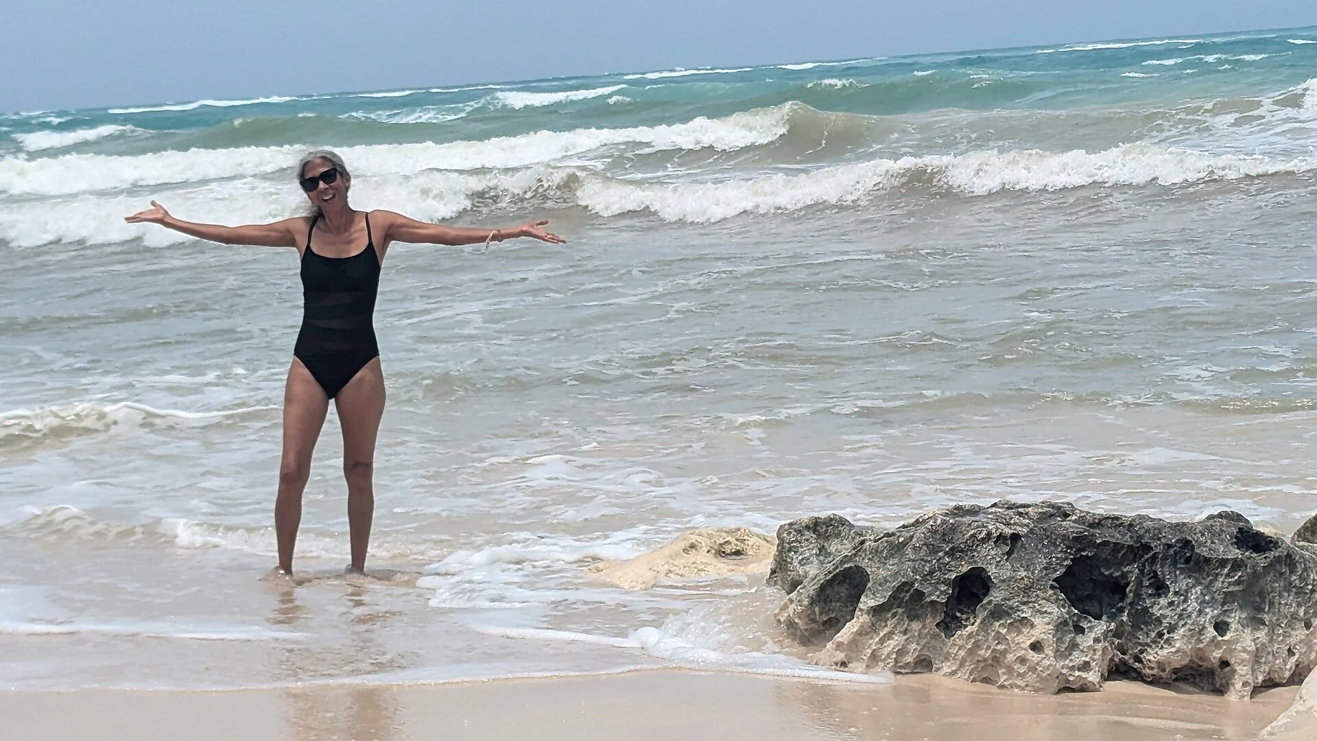 Viajera con los brazos abiertos en la orilla de una playa de Tulum con oleaje y rocas