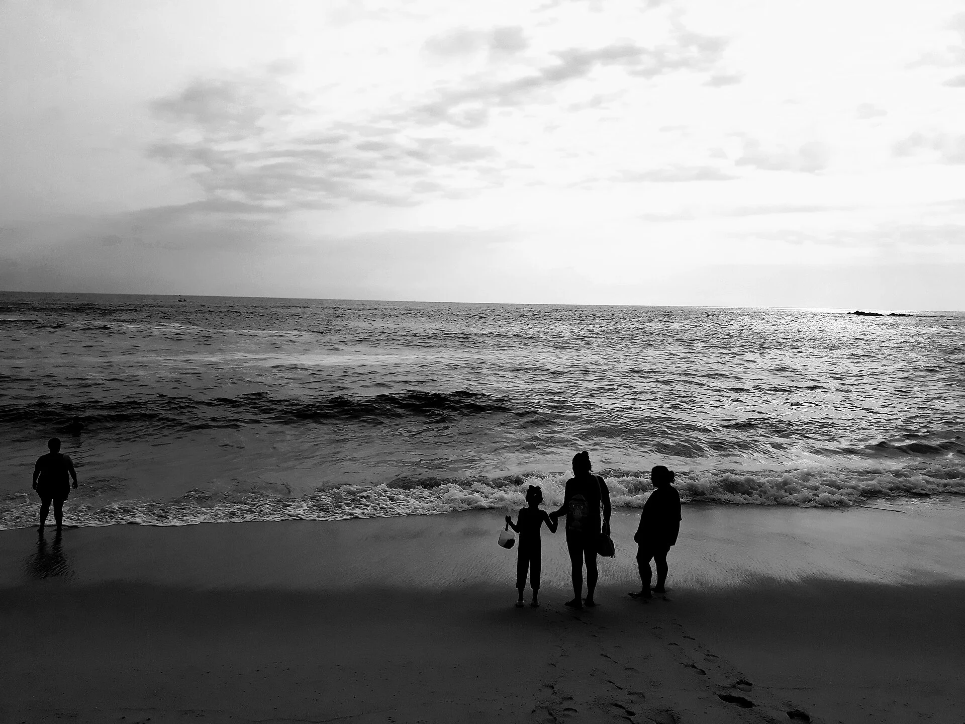 Fotografía en blanco y negro de una familia en silueta frente al oleaje en una playa de Puerto Escondido