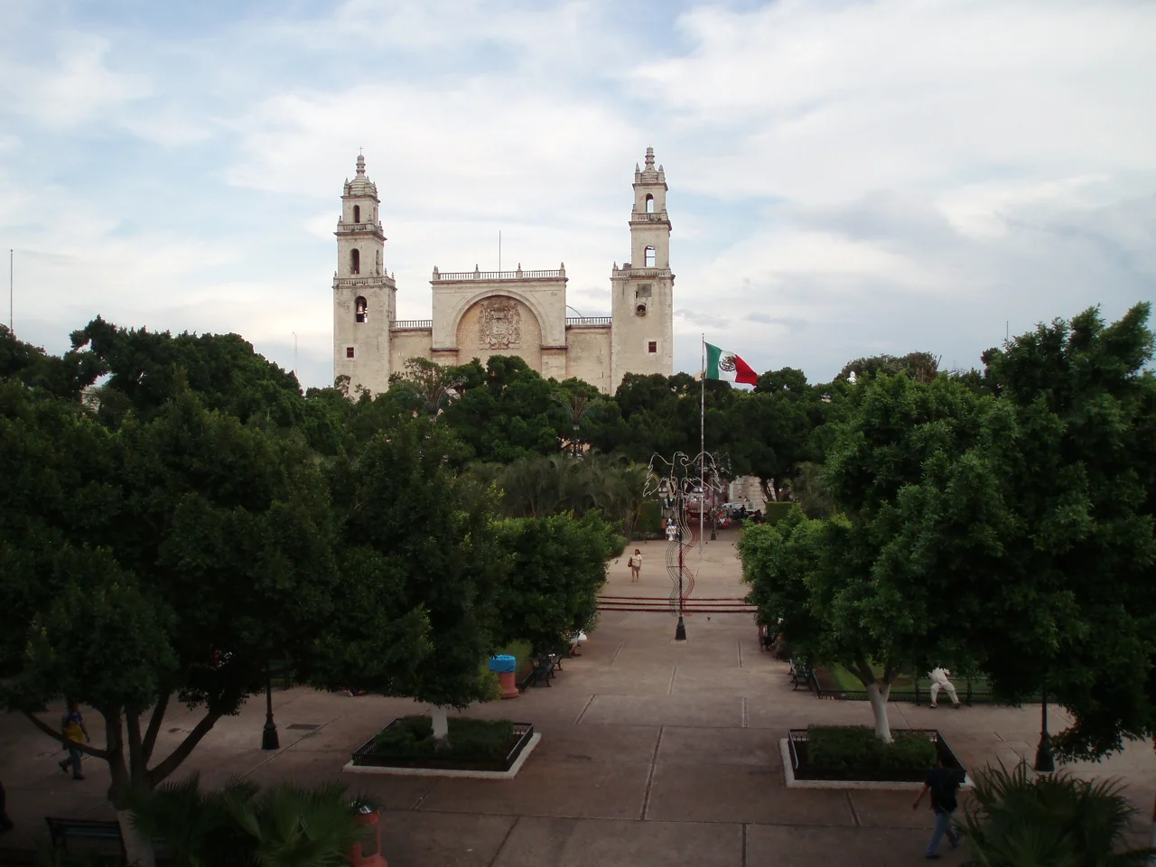 Catedral de Mérida vista desde la Plaza Grande, con árboles y la bandera de México