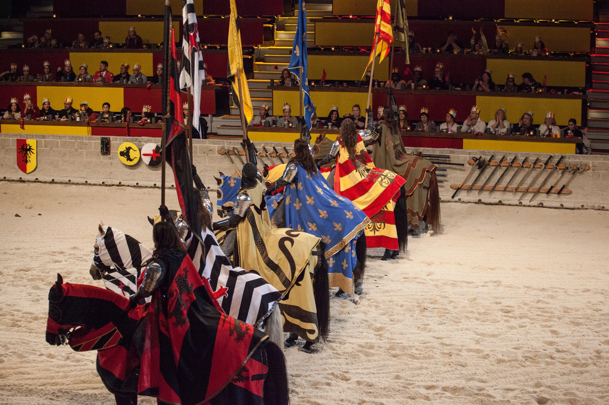 Caballeros a caballo con estandartes de colores en la arena de un espectáculo medieval con cena