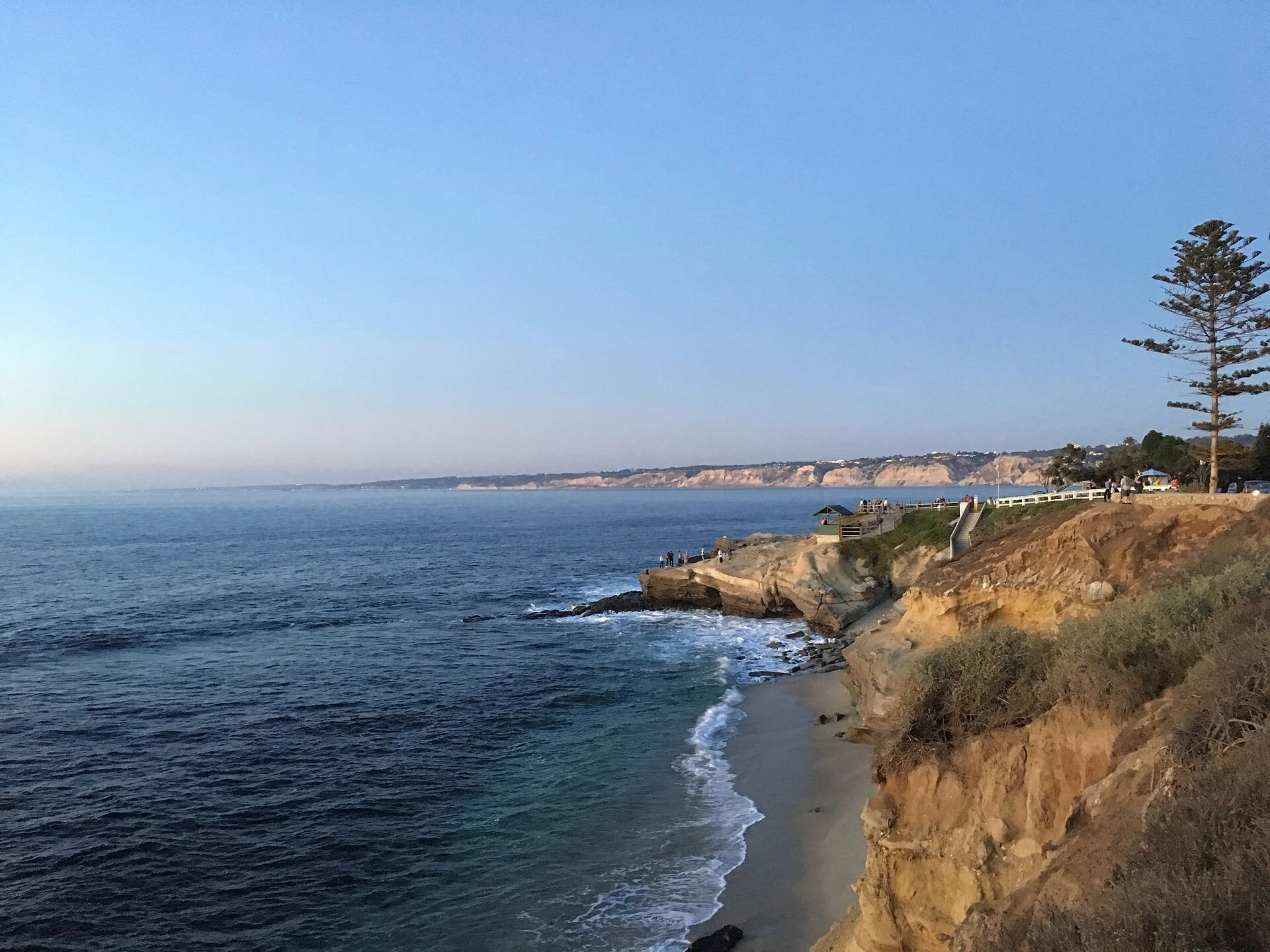 Costa de La Jolla al atardecer con acantilados dorados, una pequeña playa y el mar en calma