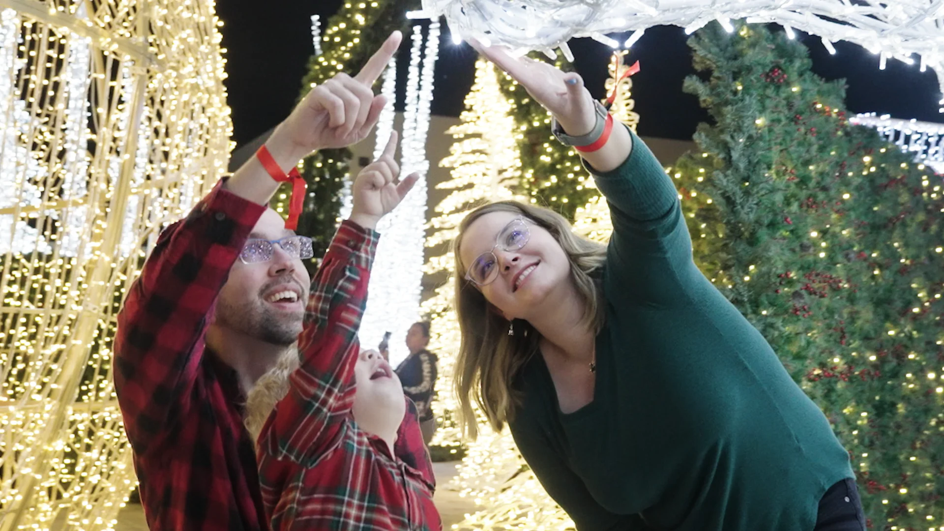 Familia con camisas de cuadros señala con asombro las luces de un festival navideño