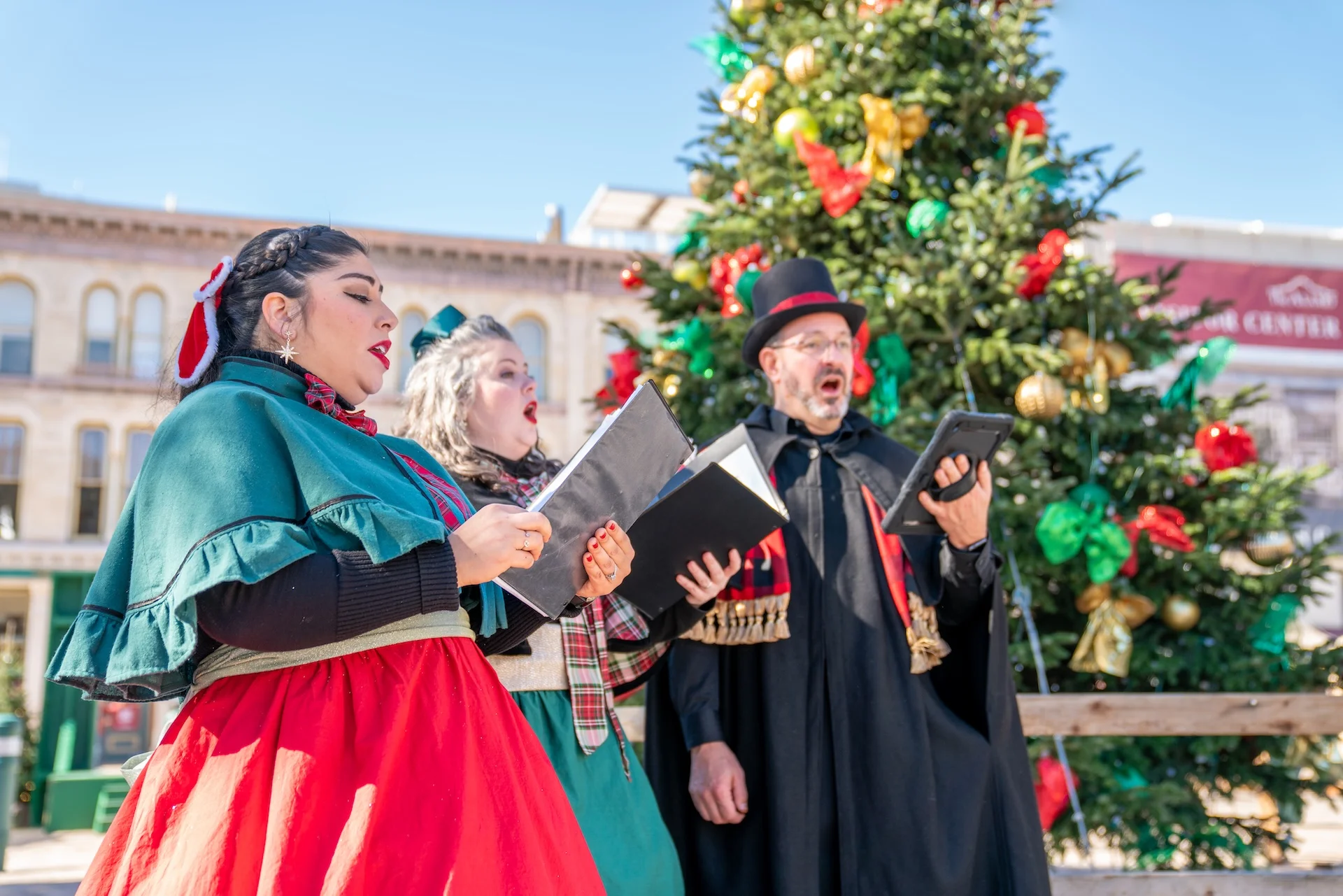 Cantantes con trajes de época interpretan villancicos frente a un árbol de Navidad