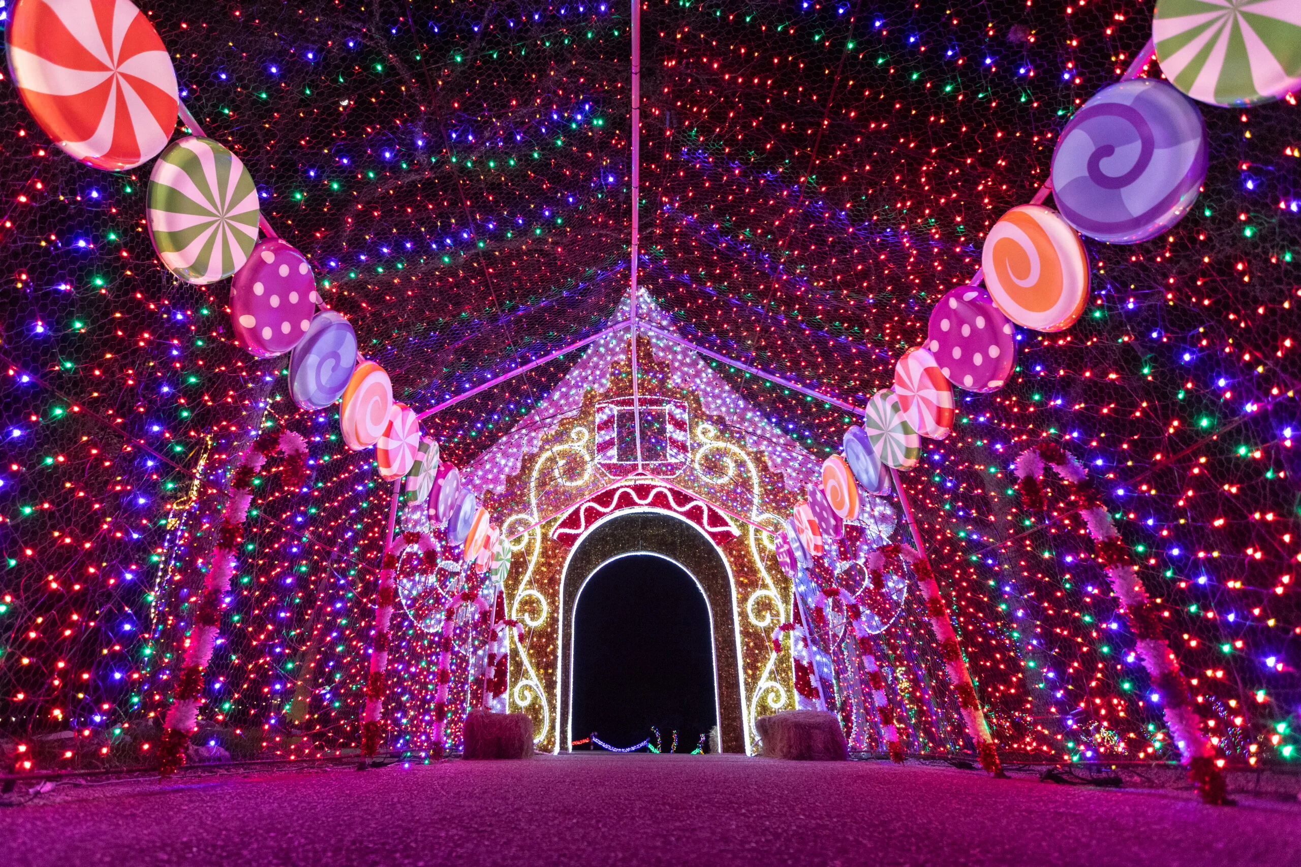 Túnel de luces navideñas decorado con dulces gigantes de colores y una casa de jengibre al fondo